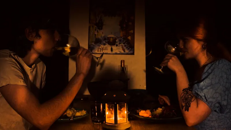 Par za stolom u polumračnoj sobi pije vino uz večeru, a između njih gori svijeća u malom fenjeru