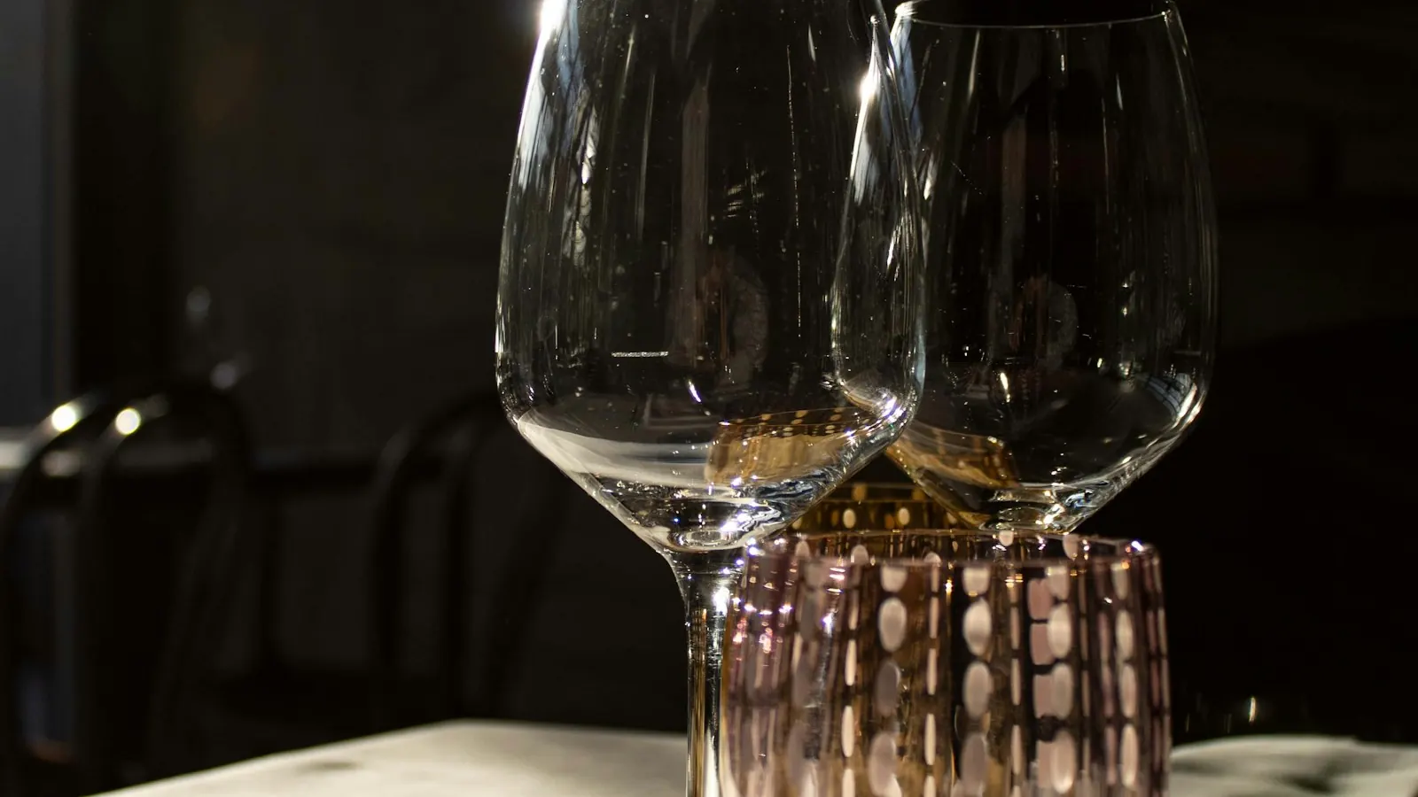 Dvije prazne čaše za vino na stolu u polumračnoj prostoriji, osvijetljene bočnim svjetlom